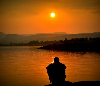 silhouette of person sitting beside body of water