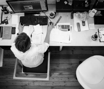 black and gray photo of person in front of computer monitor