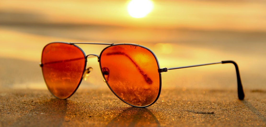 red lens sunglasses on sand near sea at sunset selective focus photography