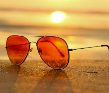 red lens sunglasses on sand near sea at sunset selective focus photography