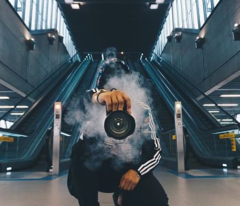 man holding camera while squating with smoke on face inside building