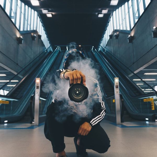 man holding camera while squating with smoke on face inside building
