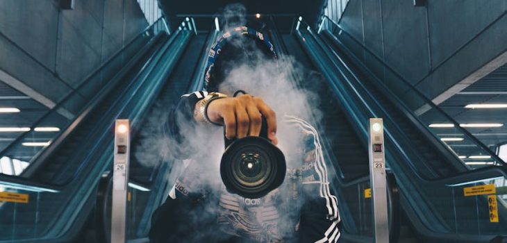 man holding camera while squating with smoke on face inside building