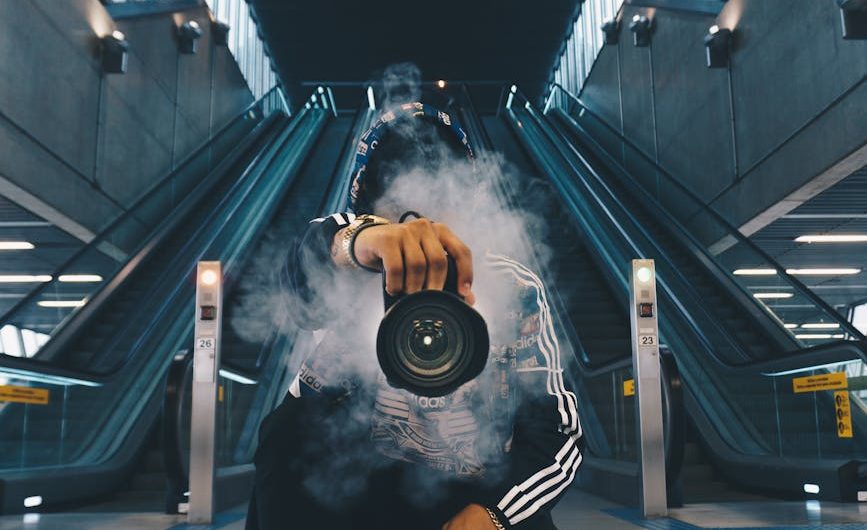 man holding camera while squating with smoke on face inside building