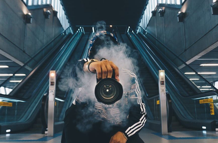 man holding camera while squating with smoke on face inside building